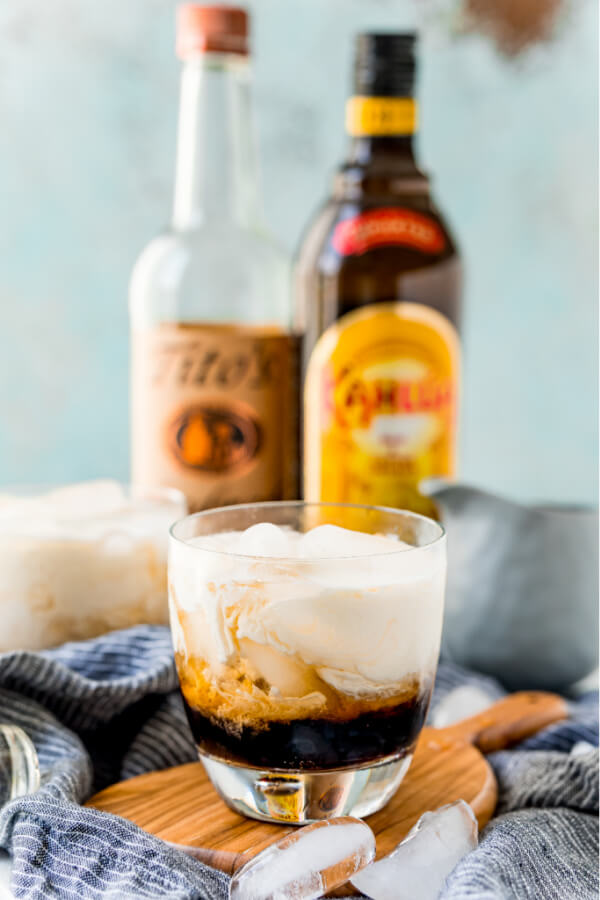 finished white russian cocktail with alcohol bottles in background