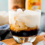 closeup of a white russian cocktail with alcohol bottle blurred in the background