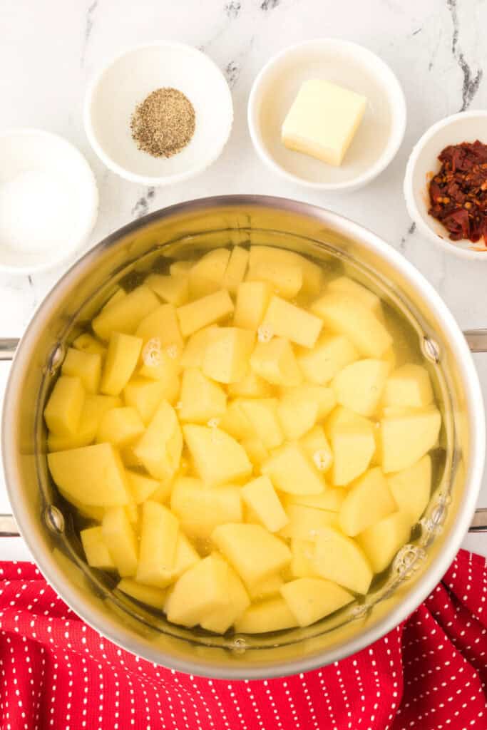 Cubed potatoes in a pot of water with measured ingredients for Chipotle Cheddar Mashed Potatoes