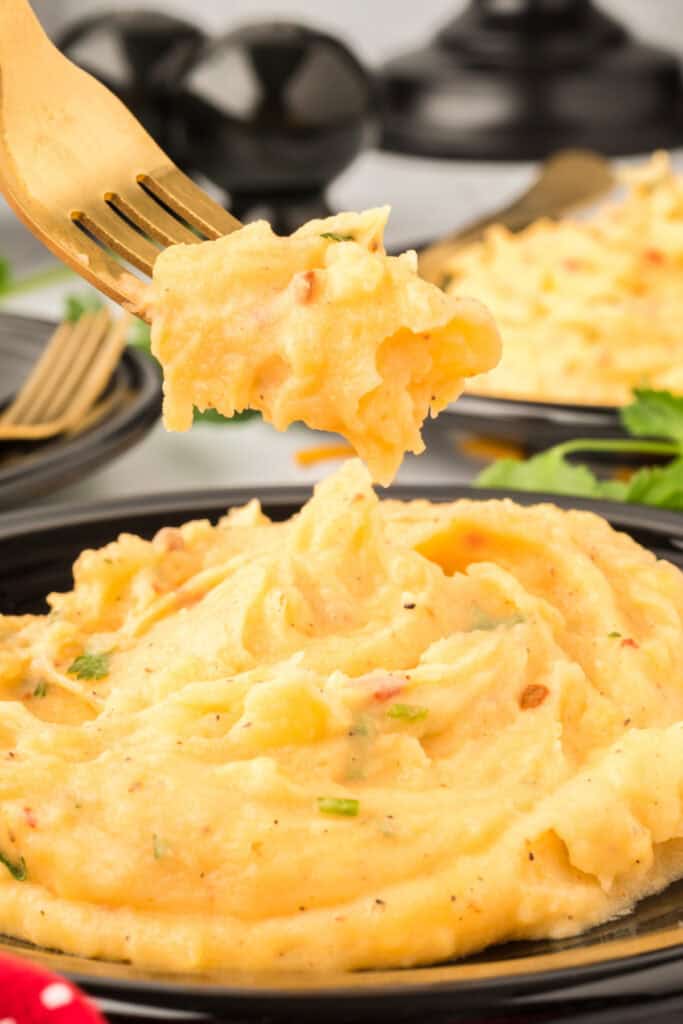 Fork lifting a bite of Chipotle Cheddar Mashed Potatoes from a serving bowl