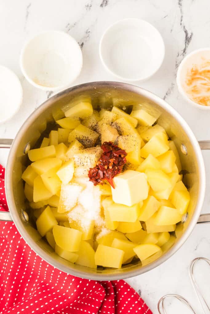 Cooked potatoes topped with butter, chipotle peppers, salt, and black pepper in a pot