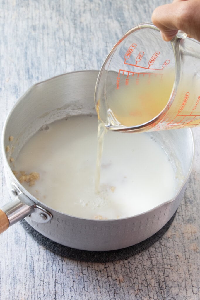 chicken broth being poured into pan with milk mixture
