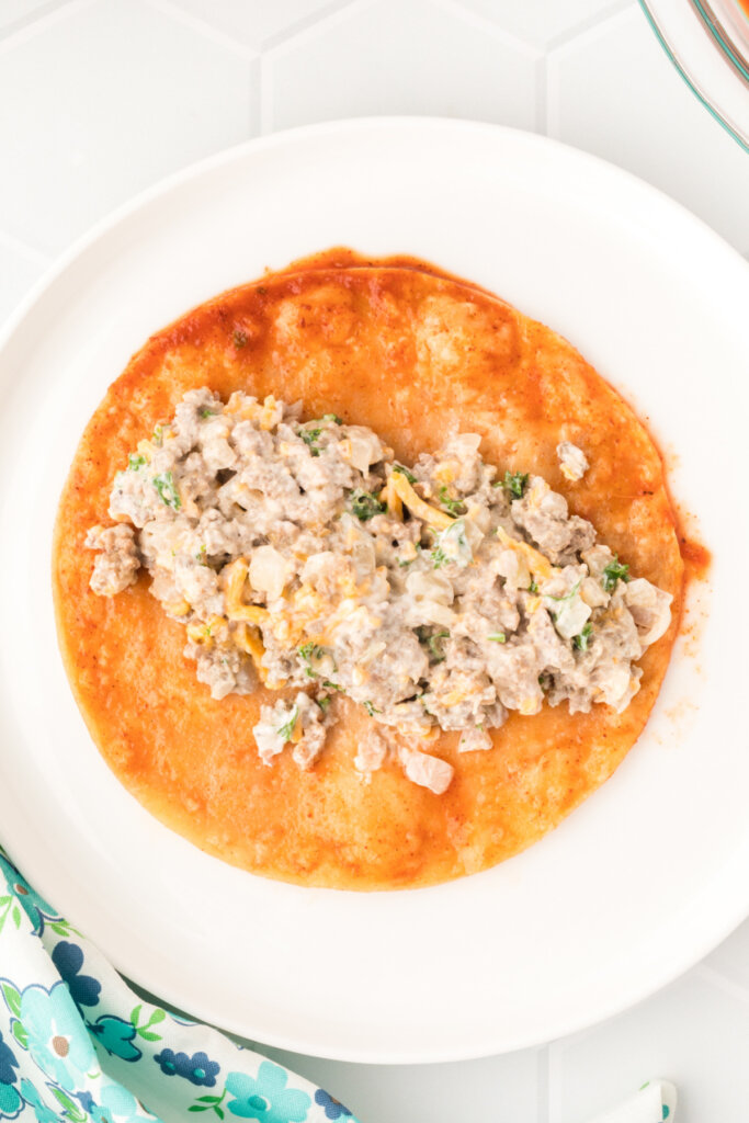 a corn tortilla being filled to make enchiladas