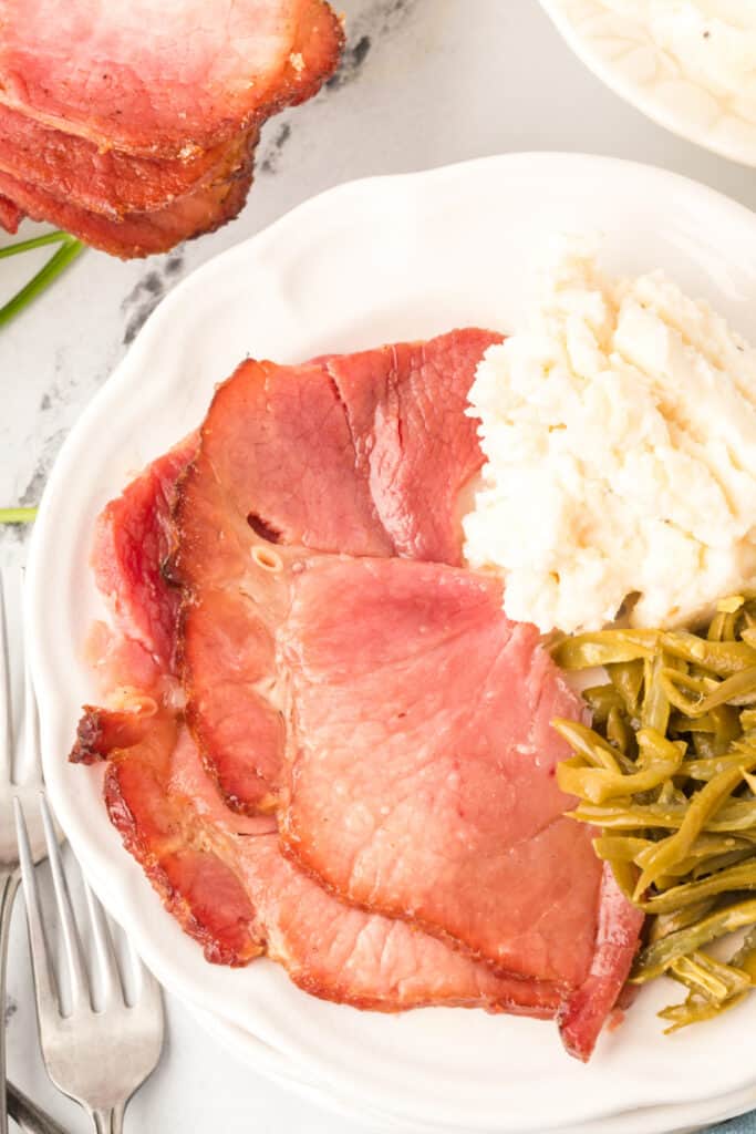 two slices of glazed ham on plate with mashed potatoes and green beans