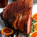honey baked ham on serving platter with orange slices and rosemary sprigs