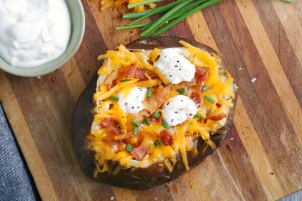 overhead of finished baked potato topped with cheese, sour cream, bacon, and chives