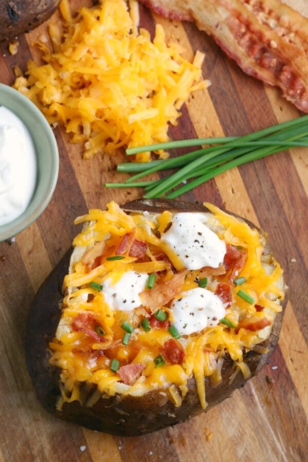 finished baked potato topped with cour cream, cheese, bacon, and chives