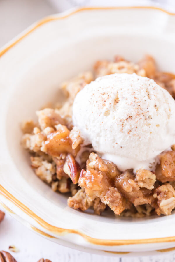 portion of apple crumble in bowl topped with ice cream scoop