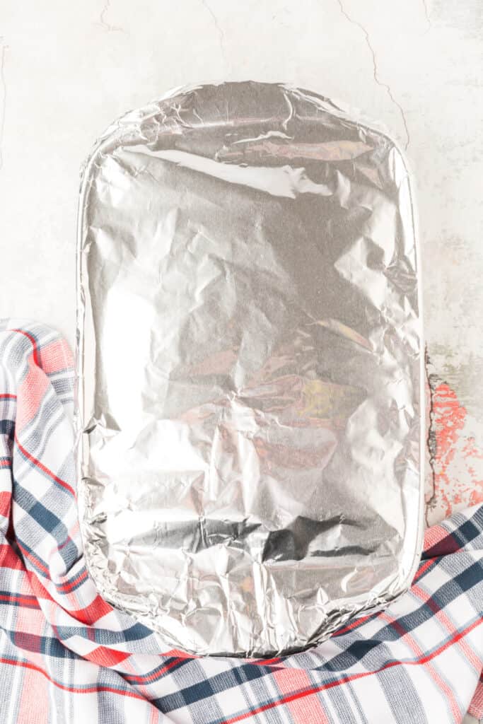 Chili Dog Casserole covered with aluminum foil in a baking dish before baking.
