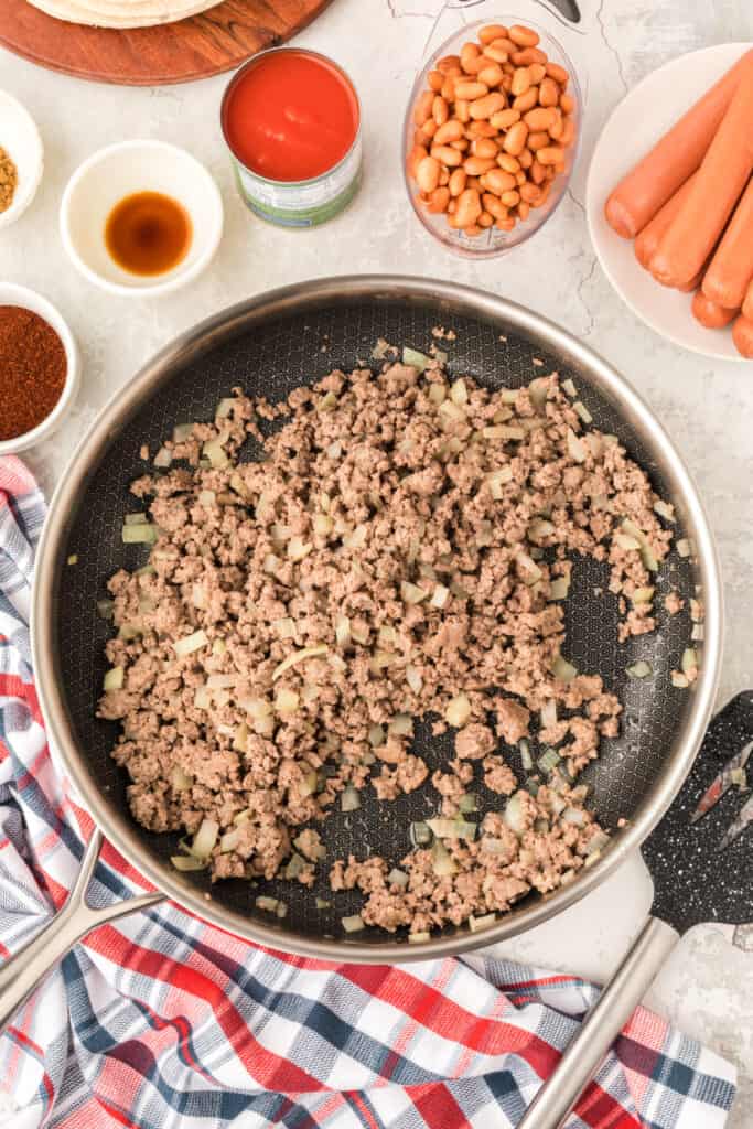 Ground beef and diced onion browned in a skillet during preparation of Chili Dog Casserole.