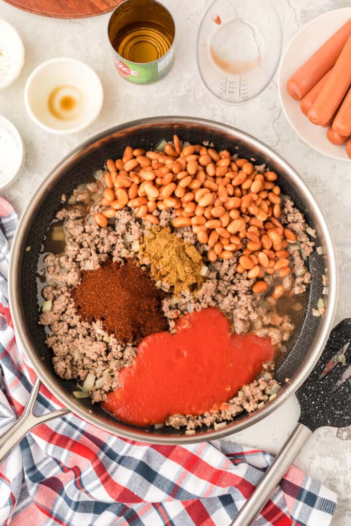 Ground beef, pinto beans, tomato sauce, water, chili powder, and cumin added to a skillet for Chili Dog Casserole.