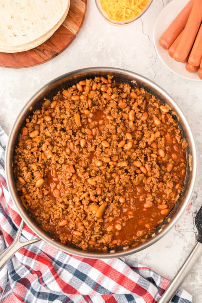 Homemade chili mixture with ground beef, onions, and pinto beans simmering in a skillet for Chili Dog Casserole.