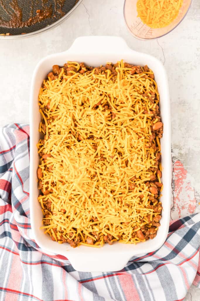 Shredded Cheddar cheese covering the chili mixture in a baking dish before baking.