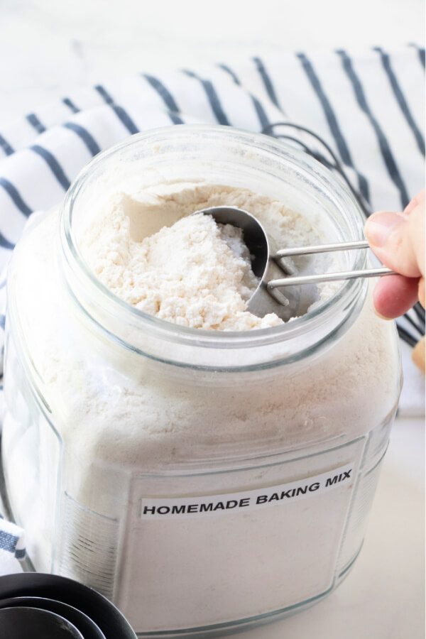 measuring cup scooping out mix in a glass jar with homemade baking mix