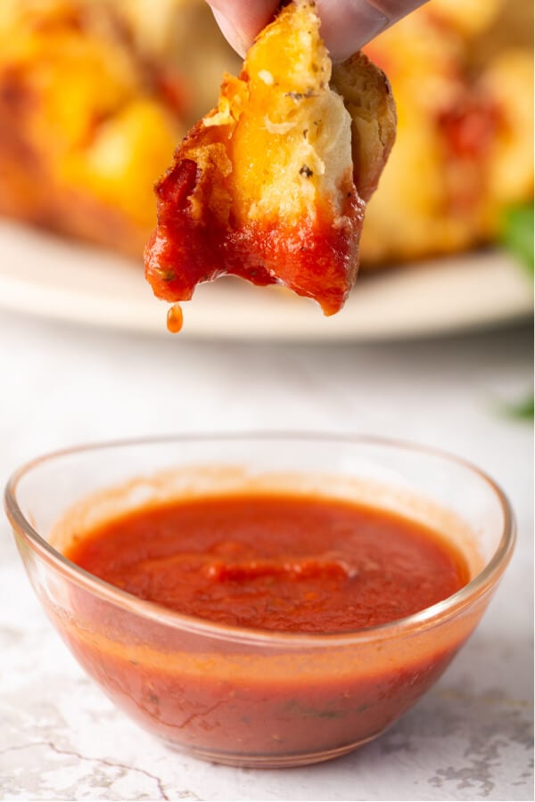 piece of bread being dipped into pizza sauce