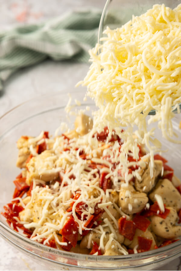 adding pepperoni and cheese to the cut up biscuits in a bowl