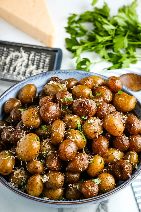 bowl of finished potatoes with fresh herbs, cheese wedge and grater in background