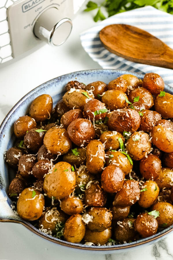 slow cooker garlic parmesan potatoes in serving bowl with crockpot and wooden spoon in background