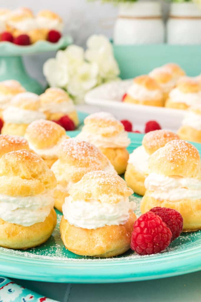 several cream puffs on teal plate with fresh raspberries