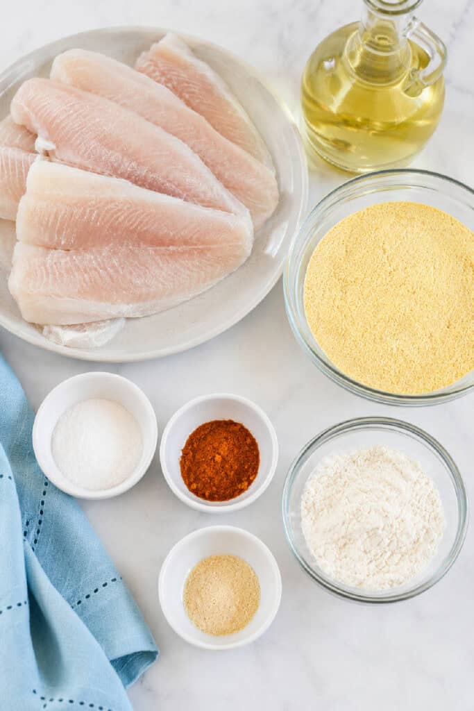 Ingredients for a classic fried fish recipe including fish fillets, cornmeal, flour, seasonings, and oil