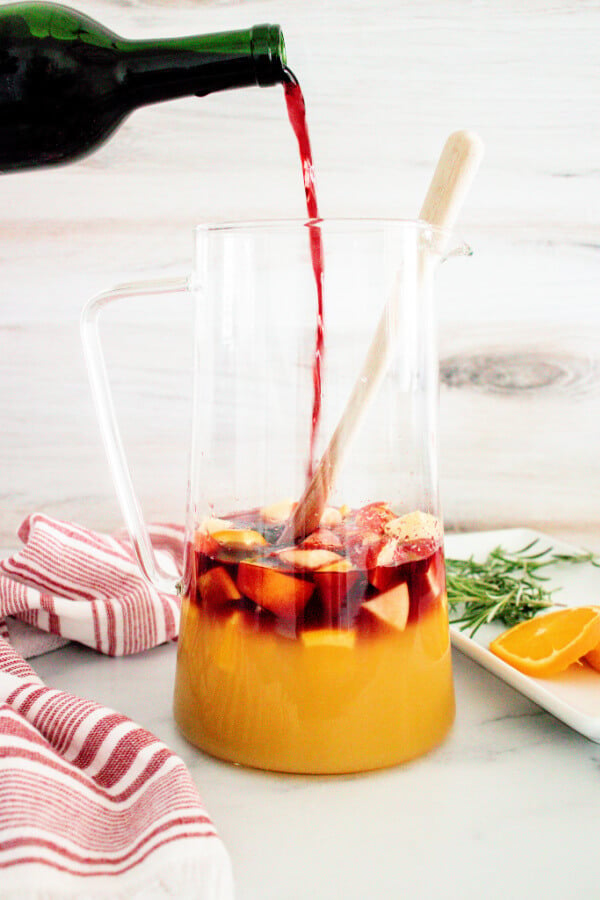 orange juice and red wine being poured over the fruit in the pitcher