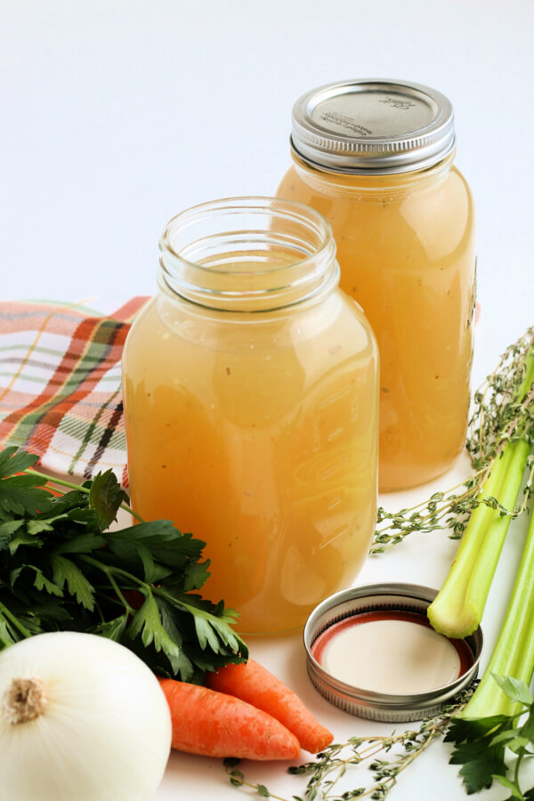 two jars of homemade stock with fresh vegetables and herbs around the jars