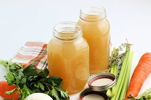 two jars of turkey stock surrounded by fresh vegetables and herbs