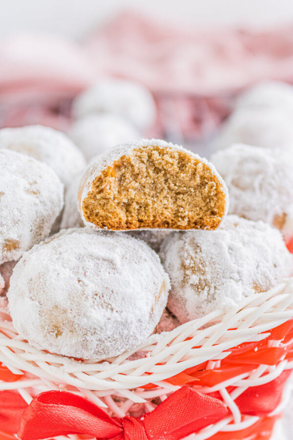 snow ball cookies stacked in a holiday basket with one cut in half so you can see the inside