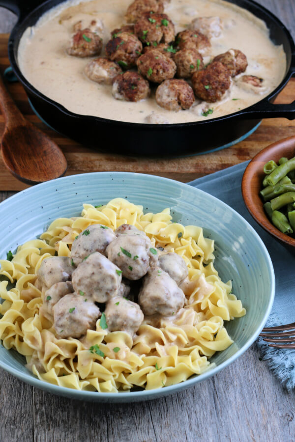 finished dish in the foreground with a pan of meatballs and gravy in the background