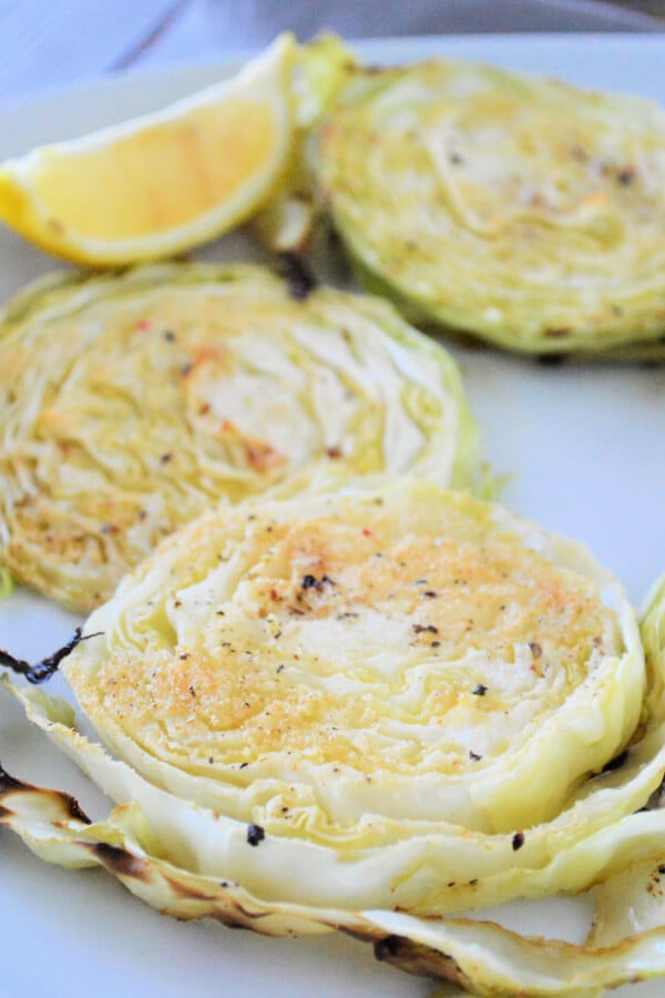 slices of roasted cabbage on a white plate with a lemon wedge