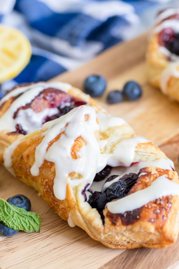 lemon blueberry danish on wooden board with fresh blueberries and blue linen