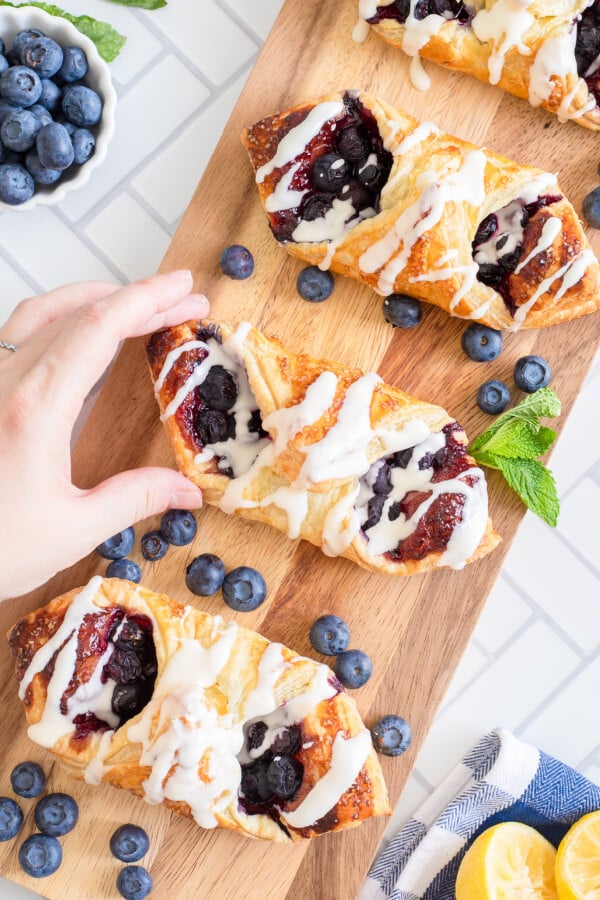 hand picking up a Lemon Blueberry Danish off of a wood board