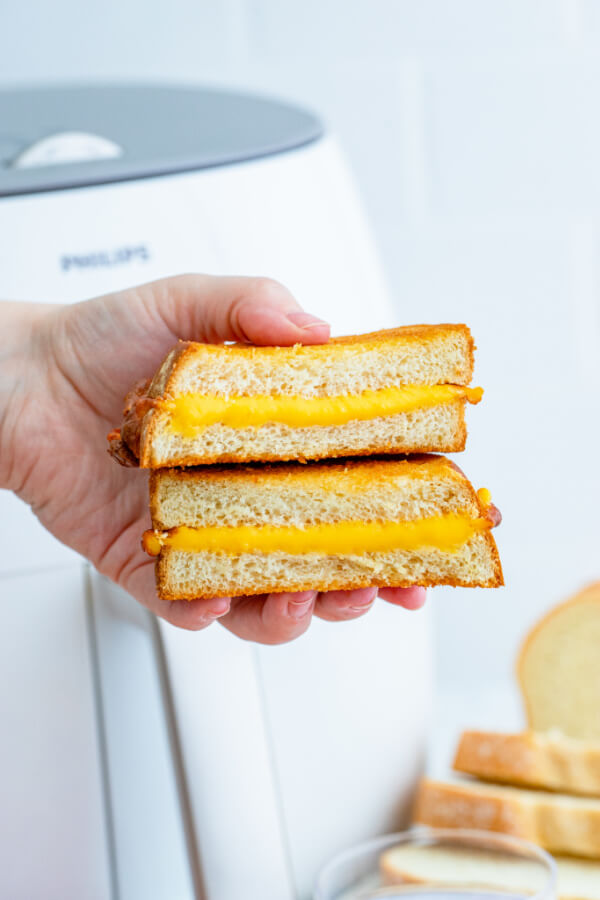 hand holding a sandwich cut in half with a white air fryer in background