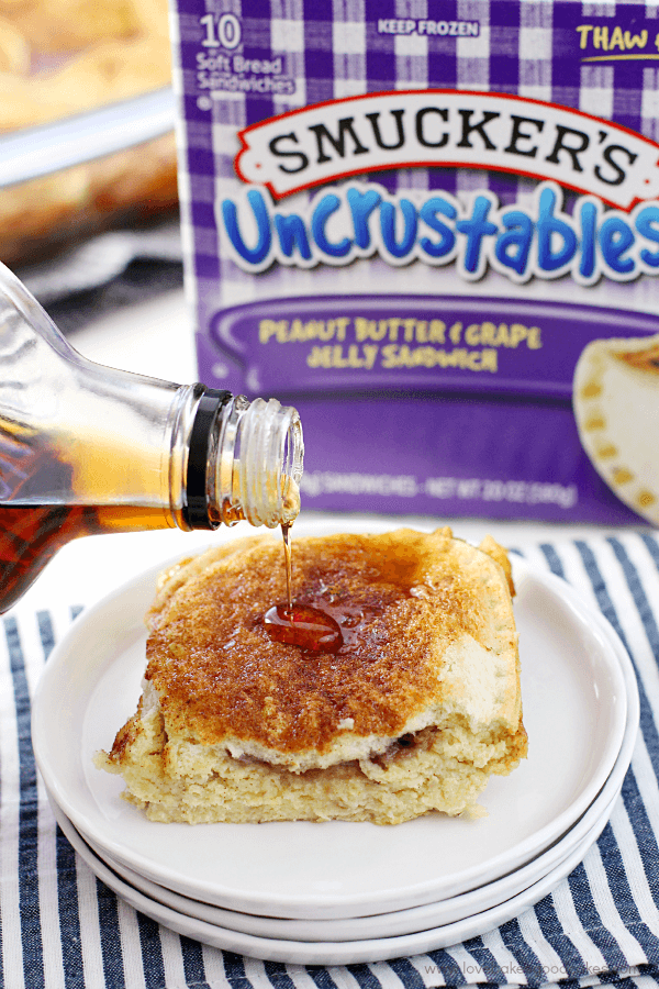 Uncrustables® Overnight French Toast on a white plate with syrup being poured over them.