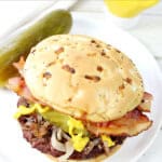 Rouladen Burger on a white plate with a pickle.