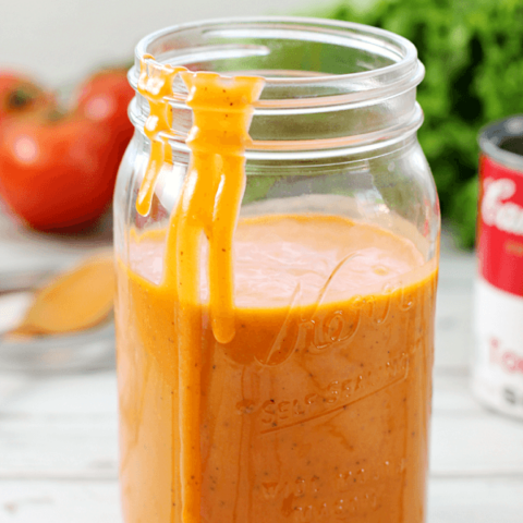 Tomato Soup Salad Dressing in a jar with the lid off and some dressing dripping down the side.