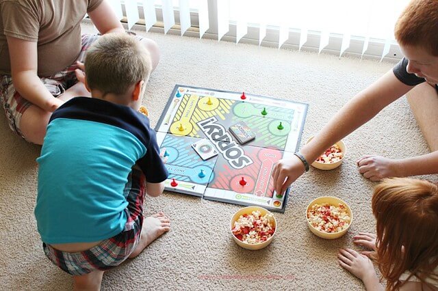 Four kids playing a board game while eating popcorn.