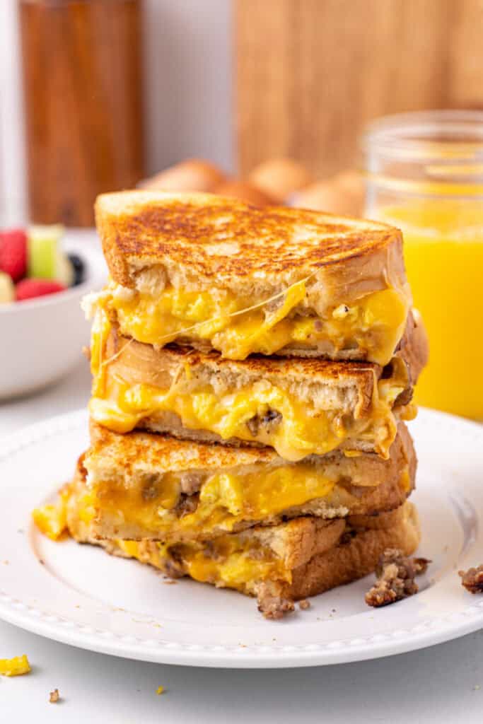 Breakfast grilled cheese sandwich cut in half on plate with melted cheese, eggs, and sausage