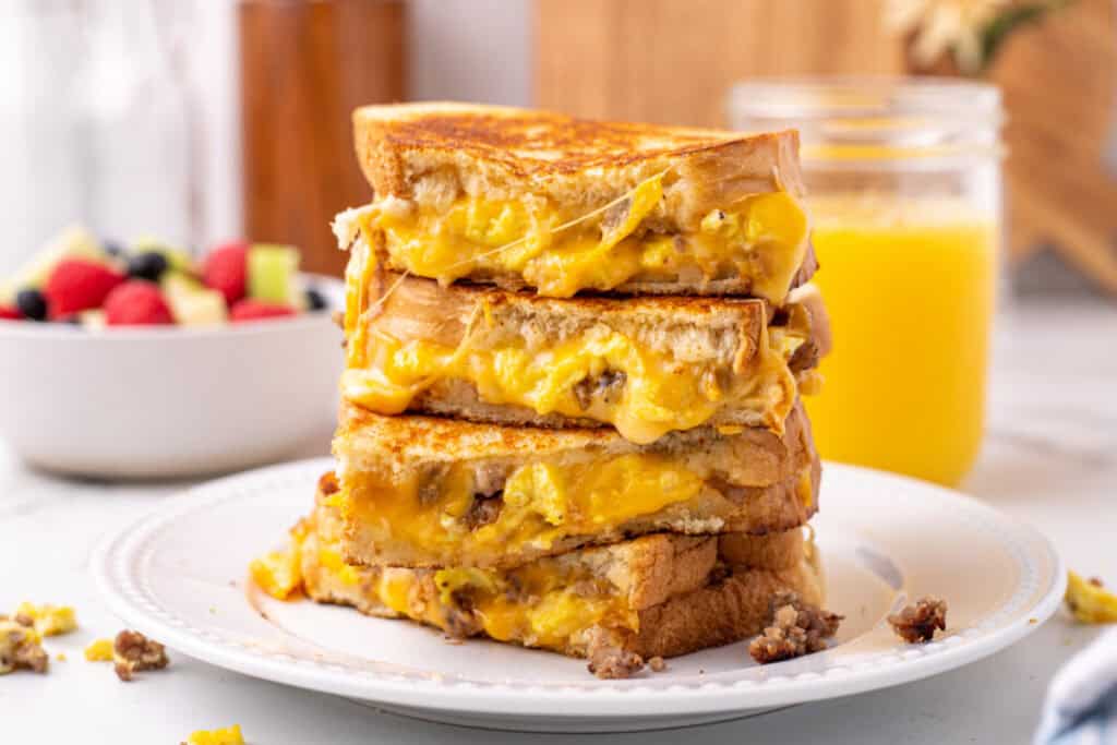 Crispy breakfast grilled cheese with eggs and sausage stacked on a plate with melted cheese