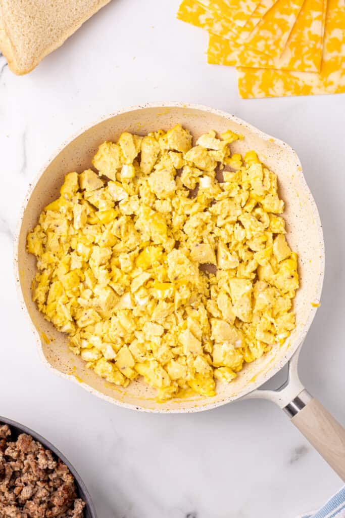 Scrambled eggs cooking in a skillet for a grilled cheese breakfast sandwich