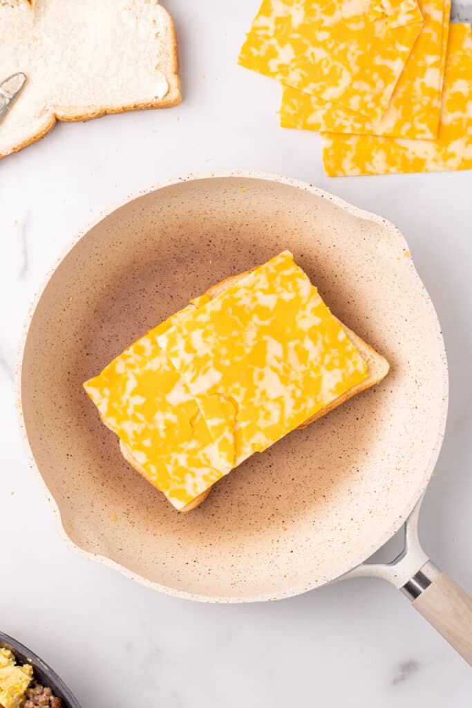 Cheese slices melting on bread for a grilled cheese breakfast sandwich with scrambled eggs