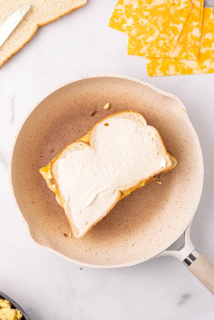 Buttered top slice added to a Breakfast Grilled Cheese sandwich in a skillet