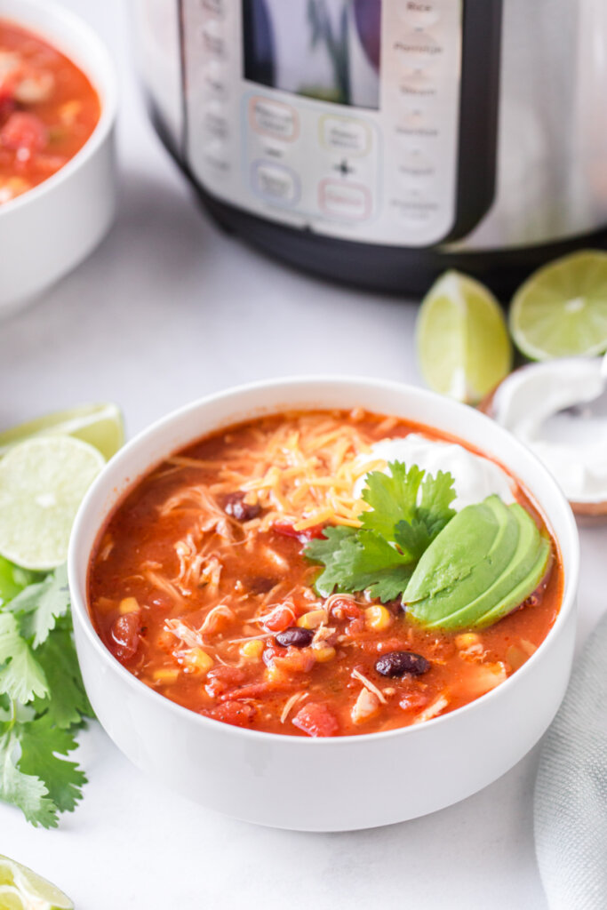 A bowl of soup with a pressure cooker in the background.