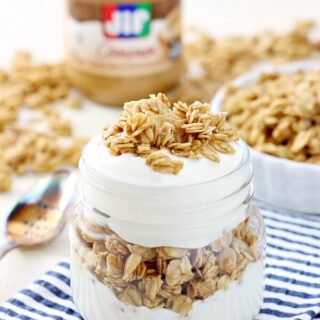 Peanut Butter Granola in a glass jar and a white bowl with a jar of Jif peanut butter.