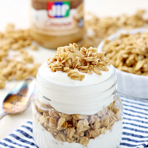 Peanut Butter Granola in a glass jar and a white bowl with a jar of Jif peanut butter.