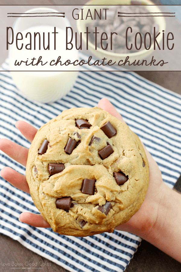 Giant Peanut Butter Cookie with Chocolate Chunks in someone's hand with a glass of milk.