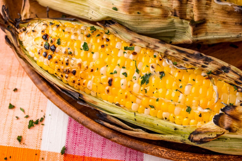 grilled corn in husk in wooden serving bowl