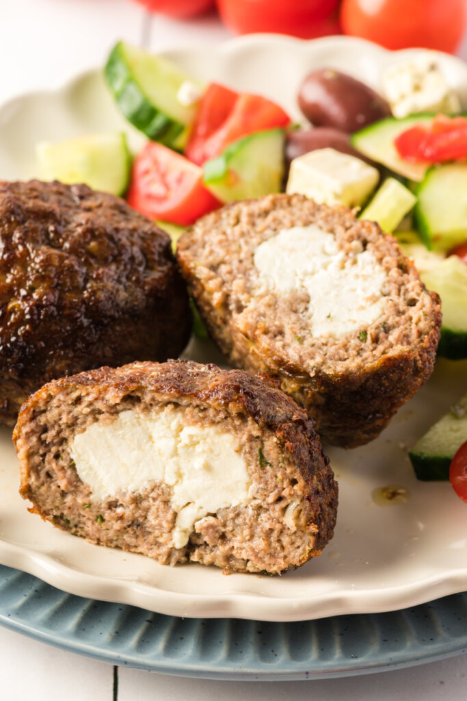 air fryer bifteki cut in half to show the feta cheese inside with greek salad in background