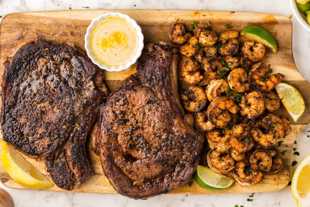 two steaks and pile of shrimp on a wooden board