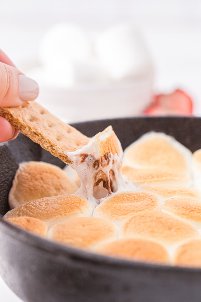 graham cracker scooping chocolate and marshmallow mixture out of cast-iron skillet